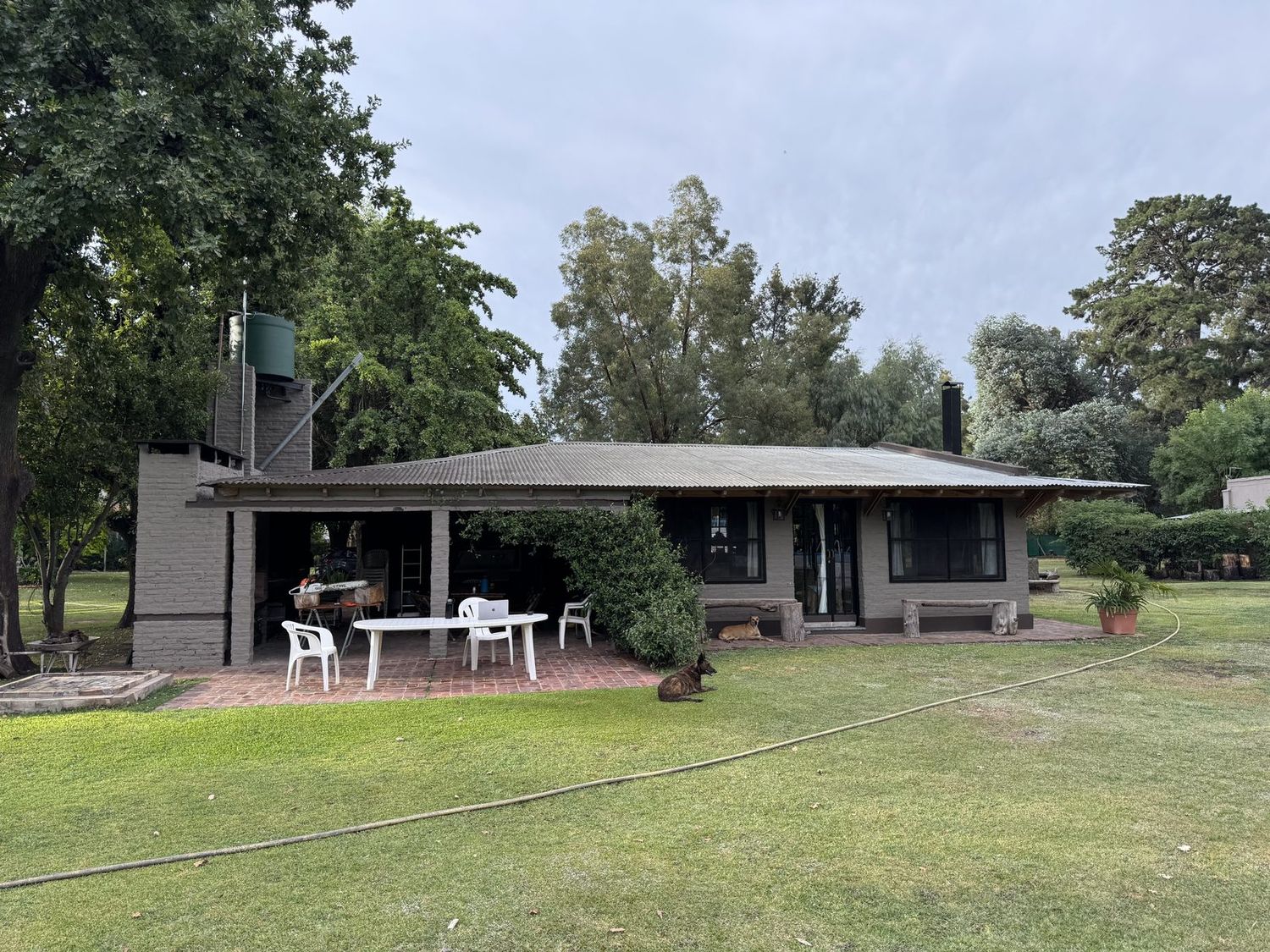 La casa vista desde el parque, con la galería, la mesa al aire libre y los árboles alrededor